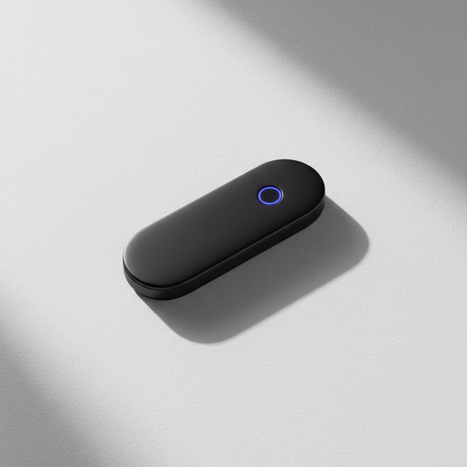 A matte-black hardware security key resting on paper-white surface, one indigo LED glowing